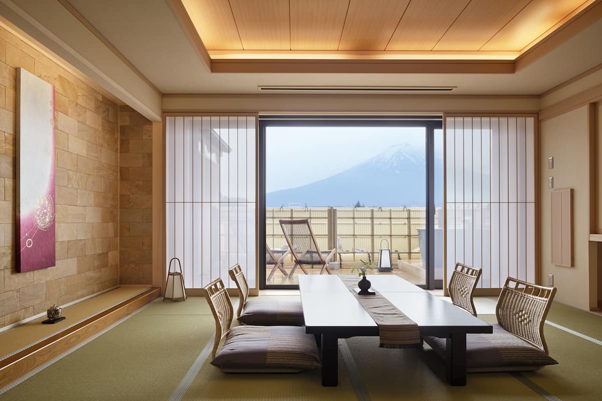 Une pièce de style japonais traditionnel, avec un sol recouvert de tatamis, une table basse avec des coussins et une vue sur une montagne, visible à travers de grandes portes coulissantes.
