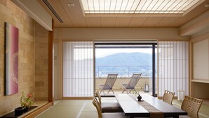A traditional Japanese room with tatami flooring, a low table, and sliding doors leading to a balcony with a view of mountains. - Konansou (Fujikawaguchiko)