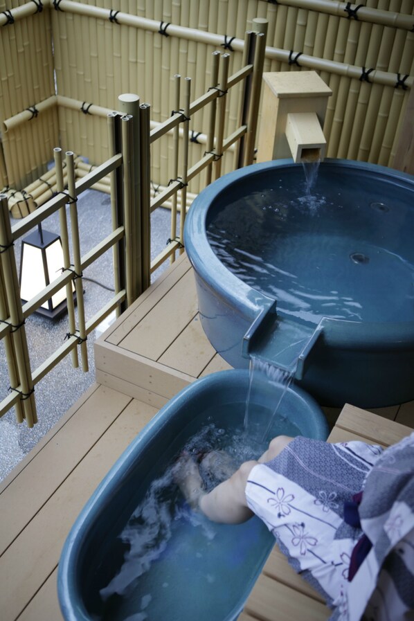 Two hot tubs with water flowing into them, surrounded by bamboo fencing and a wooden deck.