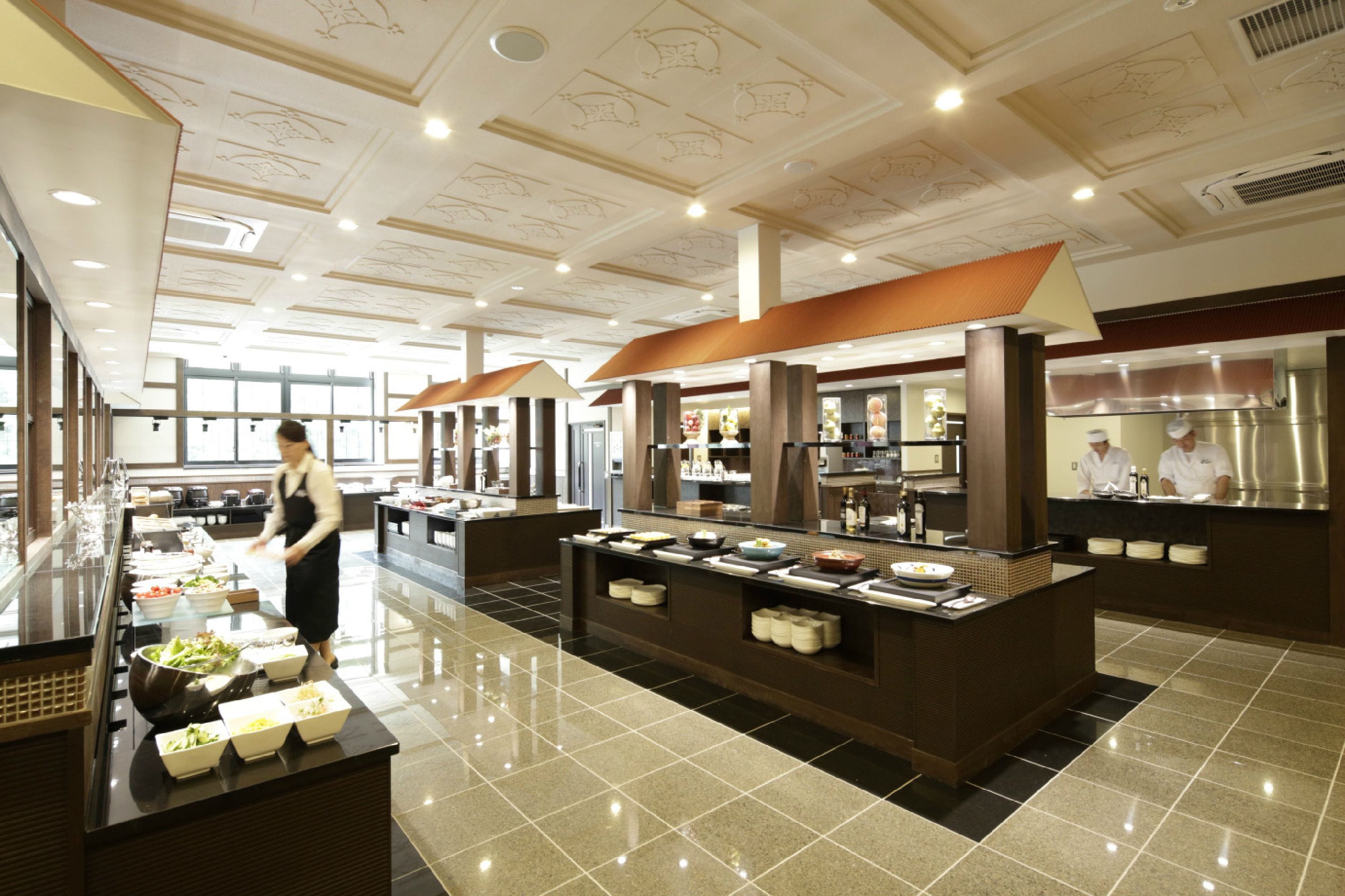A buffet area with multiple food stations, a polished floor, and a chef preparing food in the background.