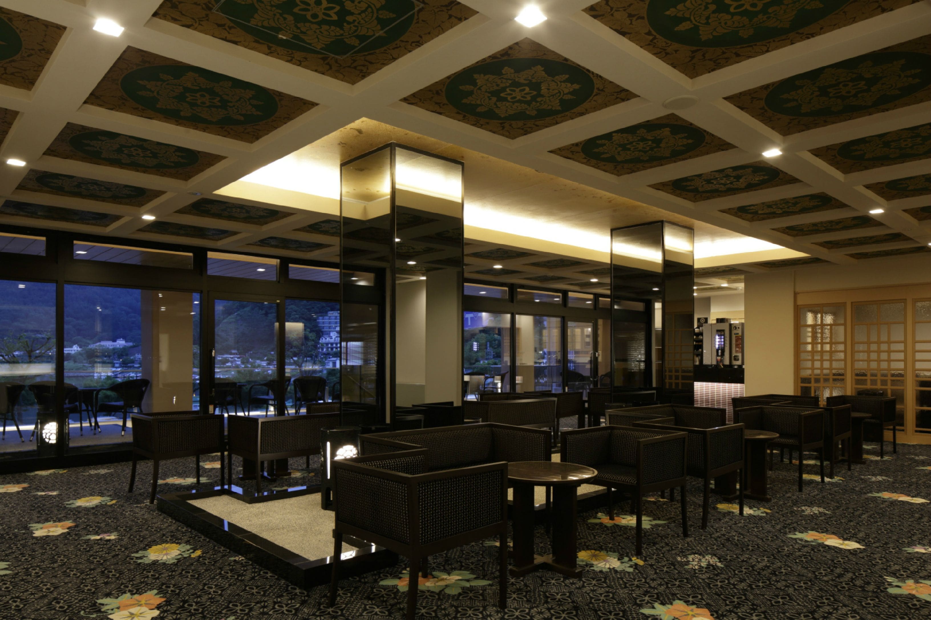 Een hotellobby met een klassiek ontwerp, met een patroon vloerkleed, donker houten meubilair en uitzicht op de stad door grote ramen.