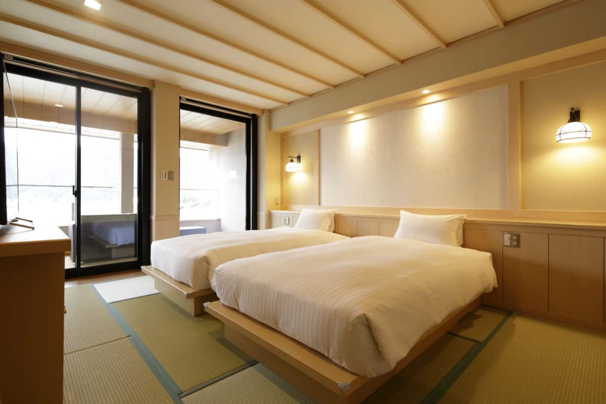 Une chambre d’hôtel avec deux lits, une porte coulissante donnant sur un balcon et un plafond en bois.