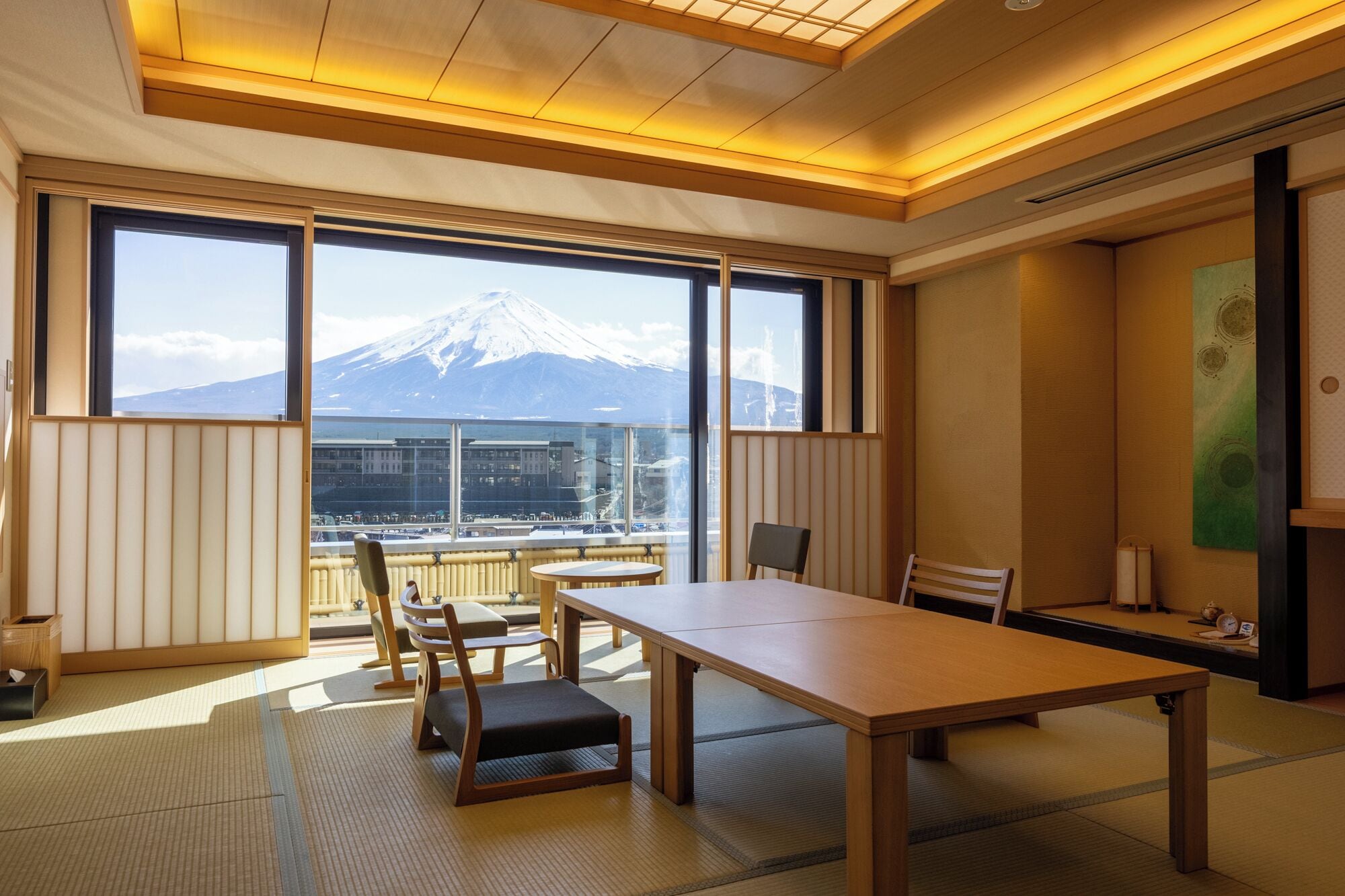A room with tatami mats, a low table, chairs, and a view of a mountain.
