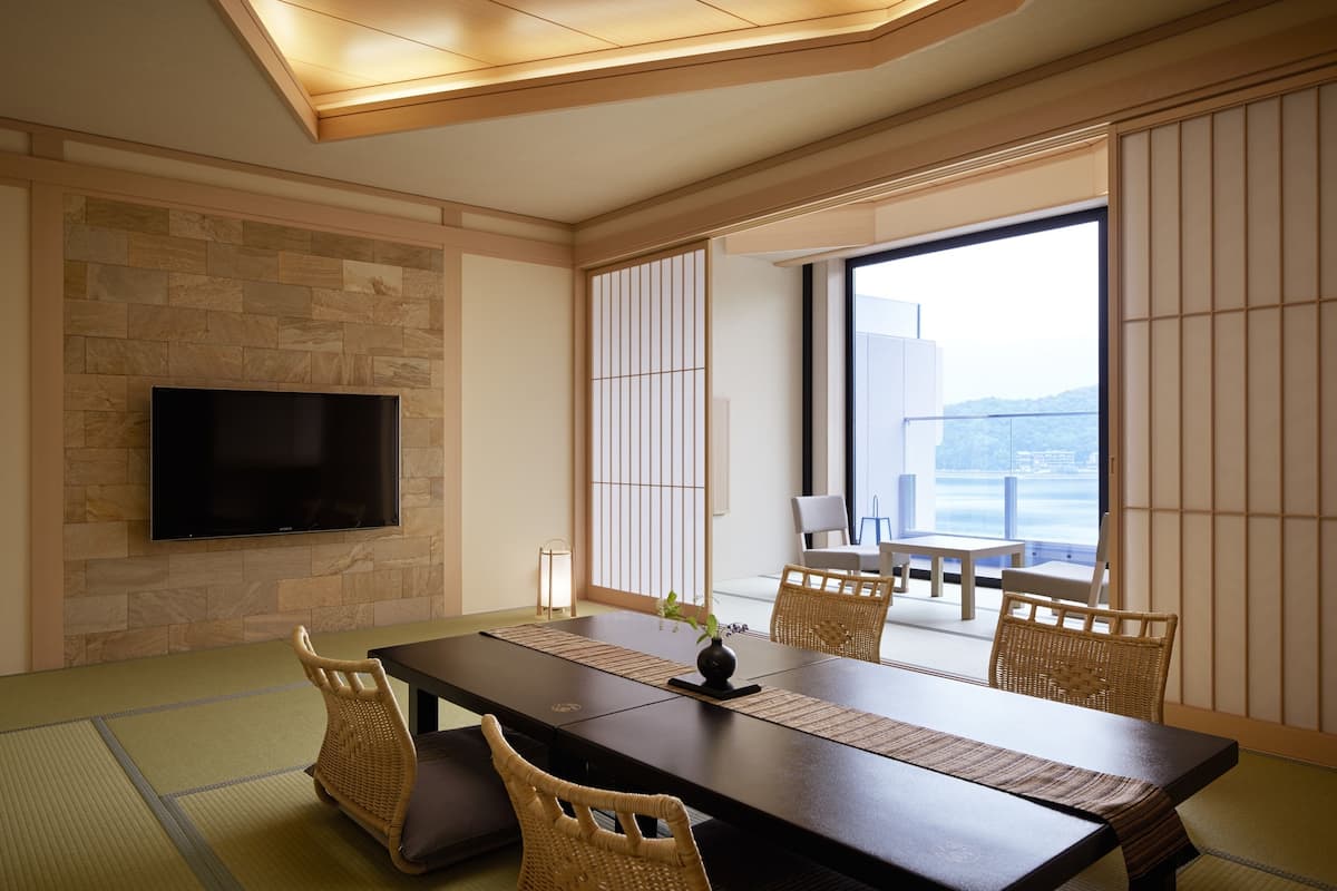 Une pièce de style japonais traditionnel, avec un sol recouvert de tatamis, une table basse et un téléviseur fixé au mur.