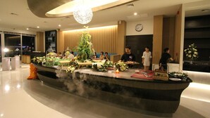 A modern restaurant with a central island featuring a decorative plant arrangement, surrounded by guests dining.