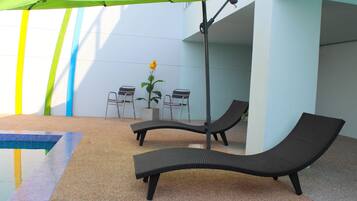 Zona de piscina con sillones de descanso, una mesa y una planta en maceta.