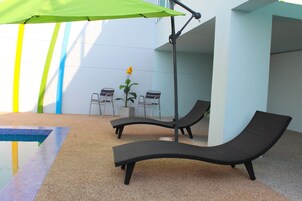 Zona de piscina con sillones de descanso, una mesa y una planta en maceta.