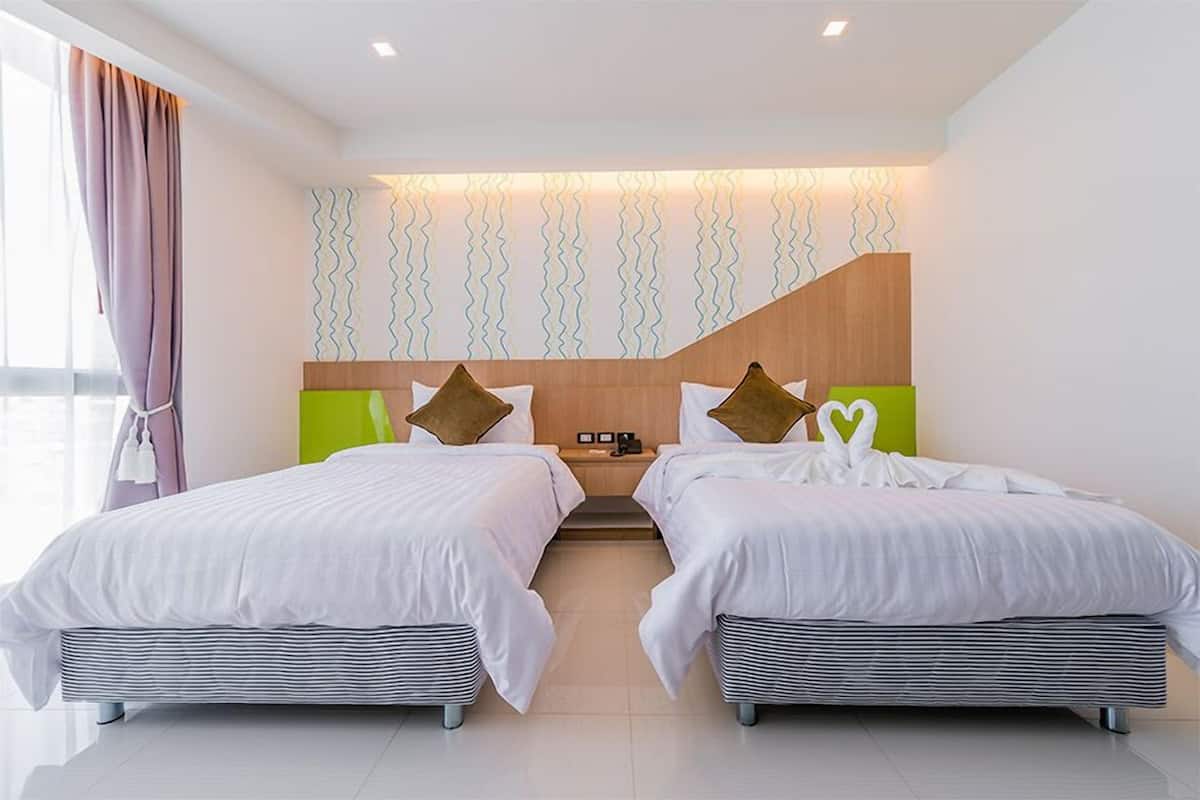 A hotel room with two beds, a wooden headboard, a wall-mounted light fixture, and a view of the outside.
