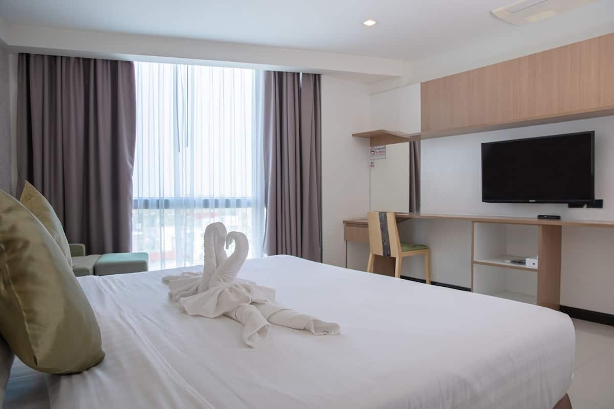 A hotel room with a large bed, a desk, a flat-screen TV, and a view of the outdoors through the window.