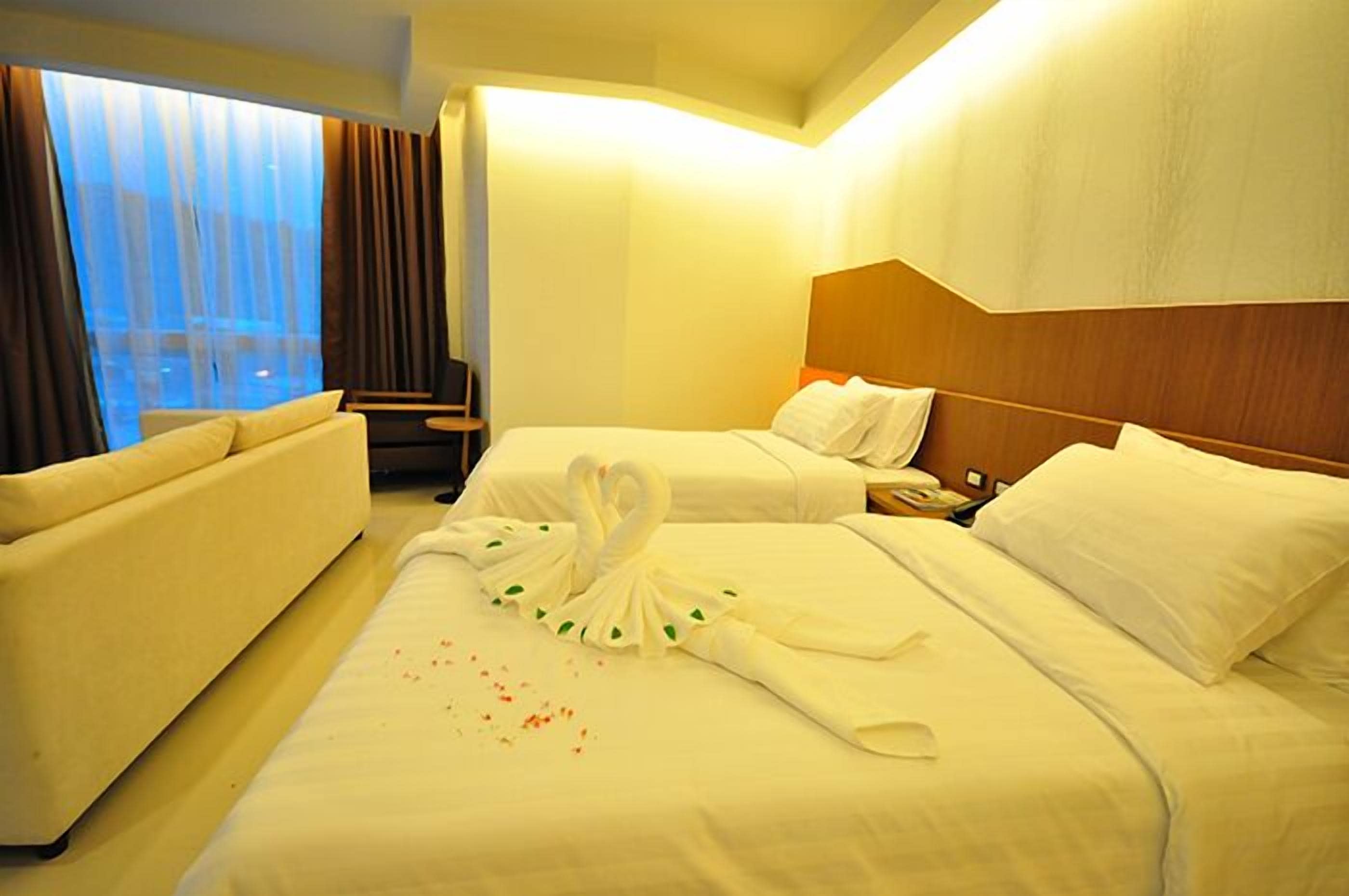 A hotel room with two beds, a sofa, a desk, and a large window with curtains.