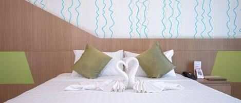 Una habitación de hotel con una cama bien hecha, almohadas verdes, un teléfono y una pequeña mesa con una libreta y un bolígrafo.