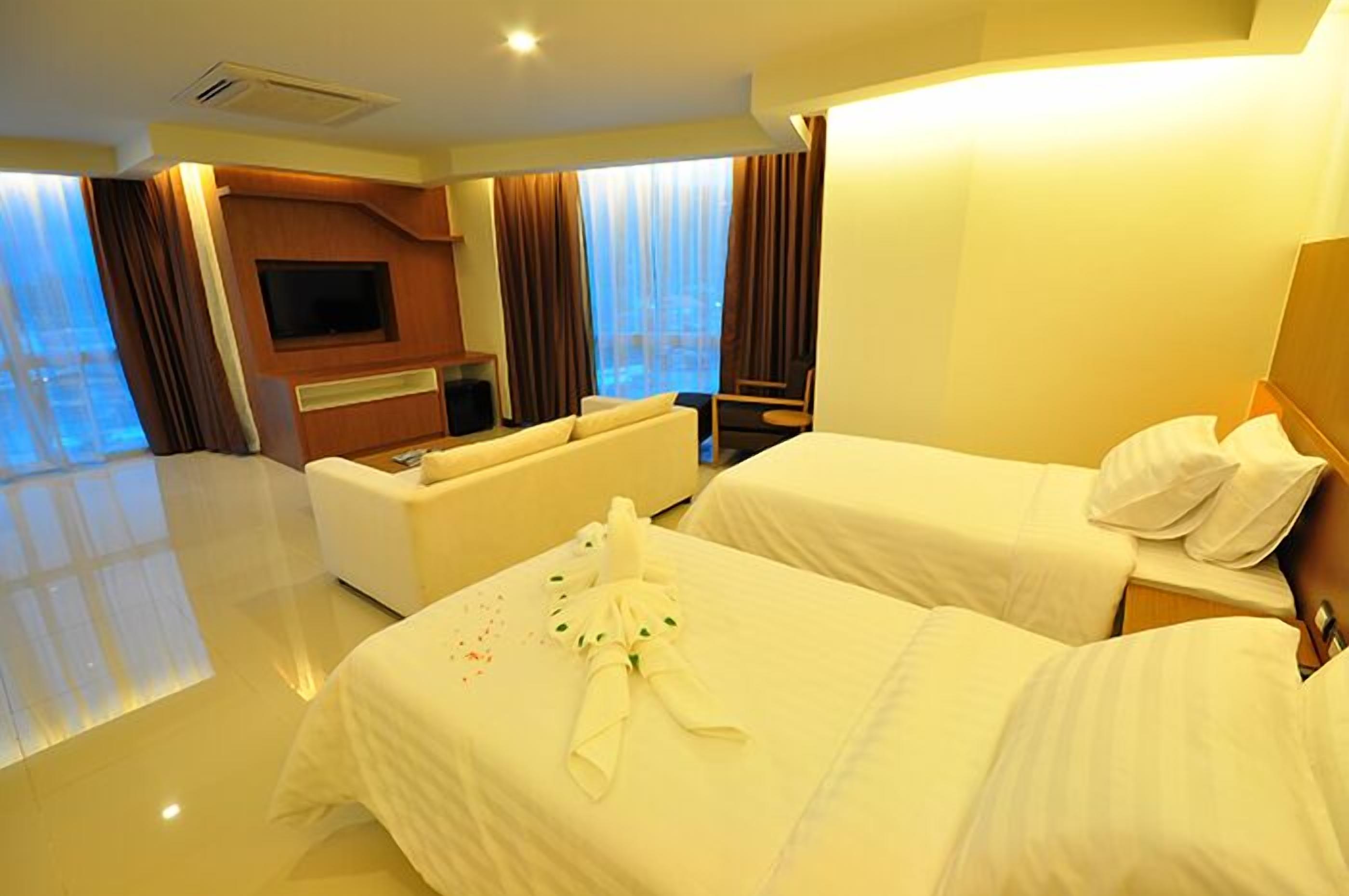 A hotel room with two beds, a sofa, a TV, and a large window with curtains.