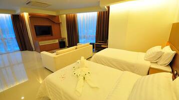 A hotel room with two beds, a sofa, a TV, and a large window with curtains.