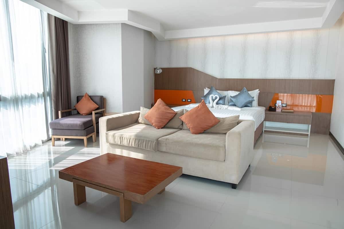 A modern hotel room with a large bed, two sofas, a coffee table, and a desk.