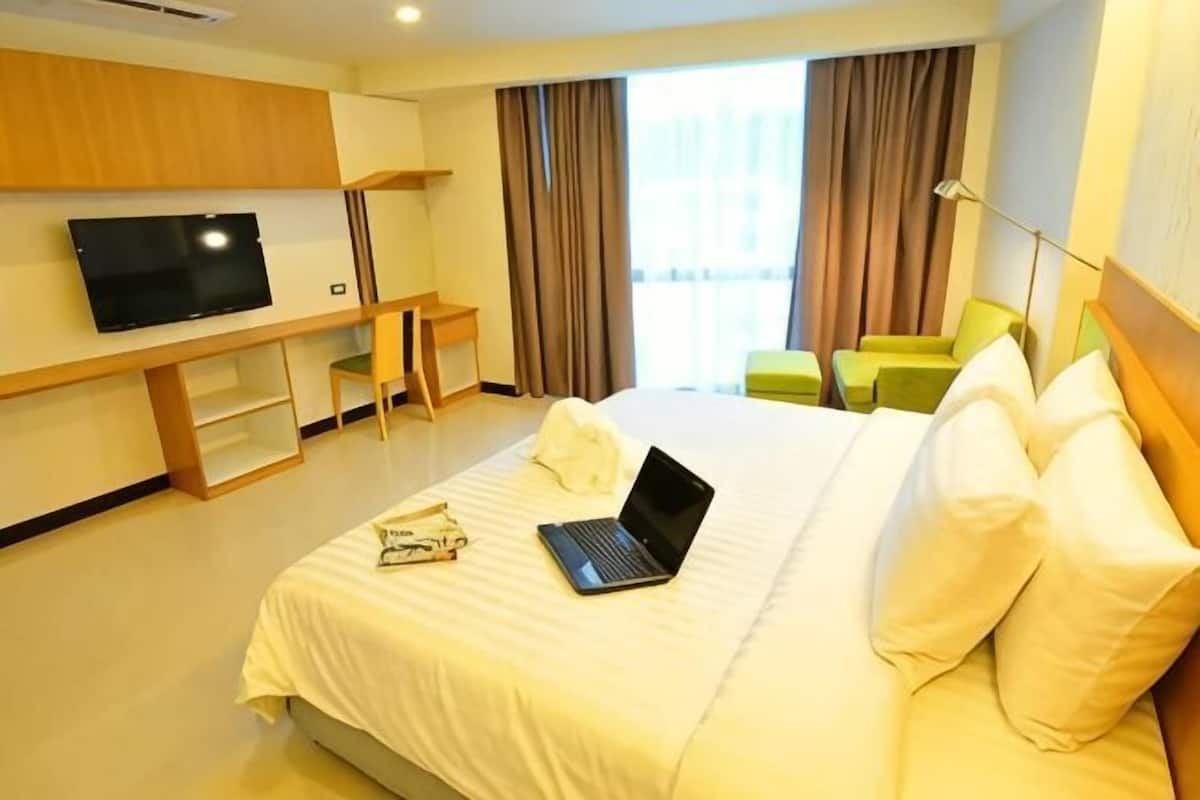 A hotel room with a bed, a desk with a laptop, a TV, and a window with curtains.