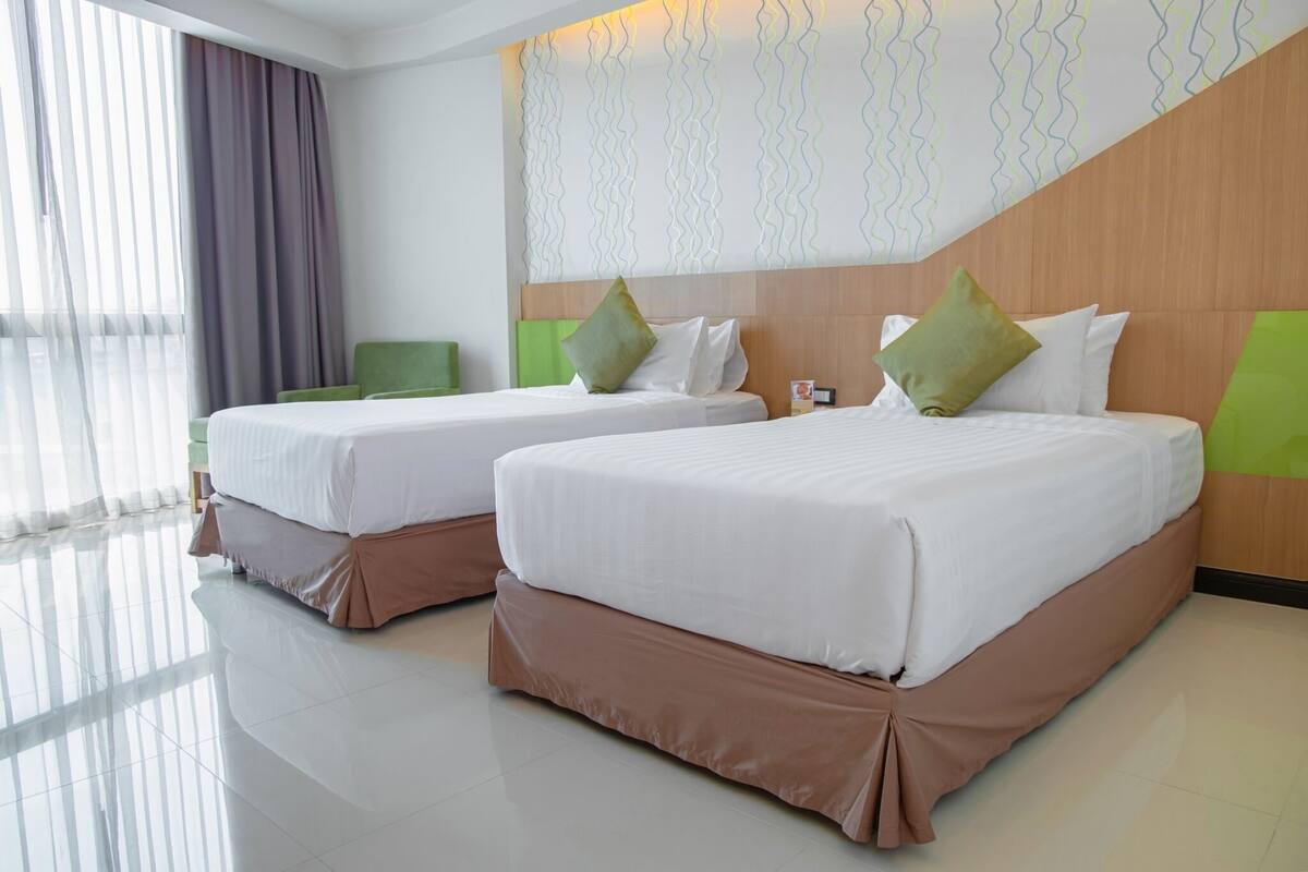 A hotel room with two beds, a wooden headboard, a large window with curtains, and a modern wall design.