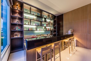 A modern kitchen with a bar area, wooden cabinets, and a variety of kitchenware and bottles.