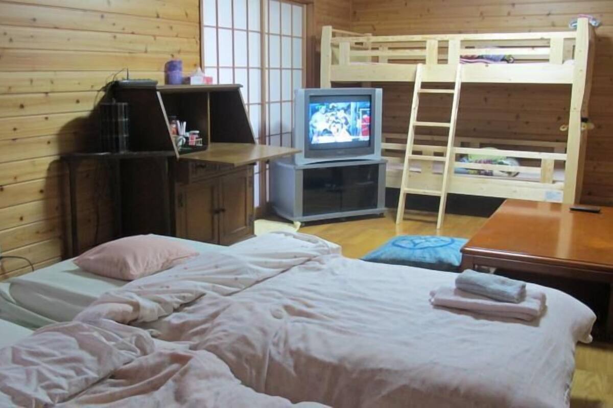 A room with two beds, a television, a desk, and a bunk bed.