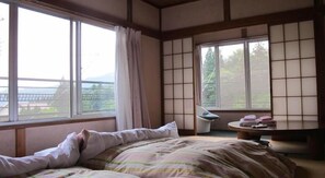 A bedroom with a bed, a bedside table, and a view of the outdoors through large windows. - Narusawa Lodge (Nikko)
