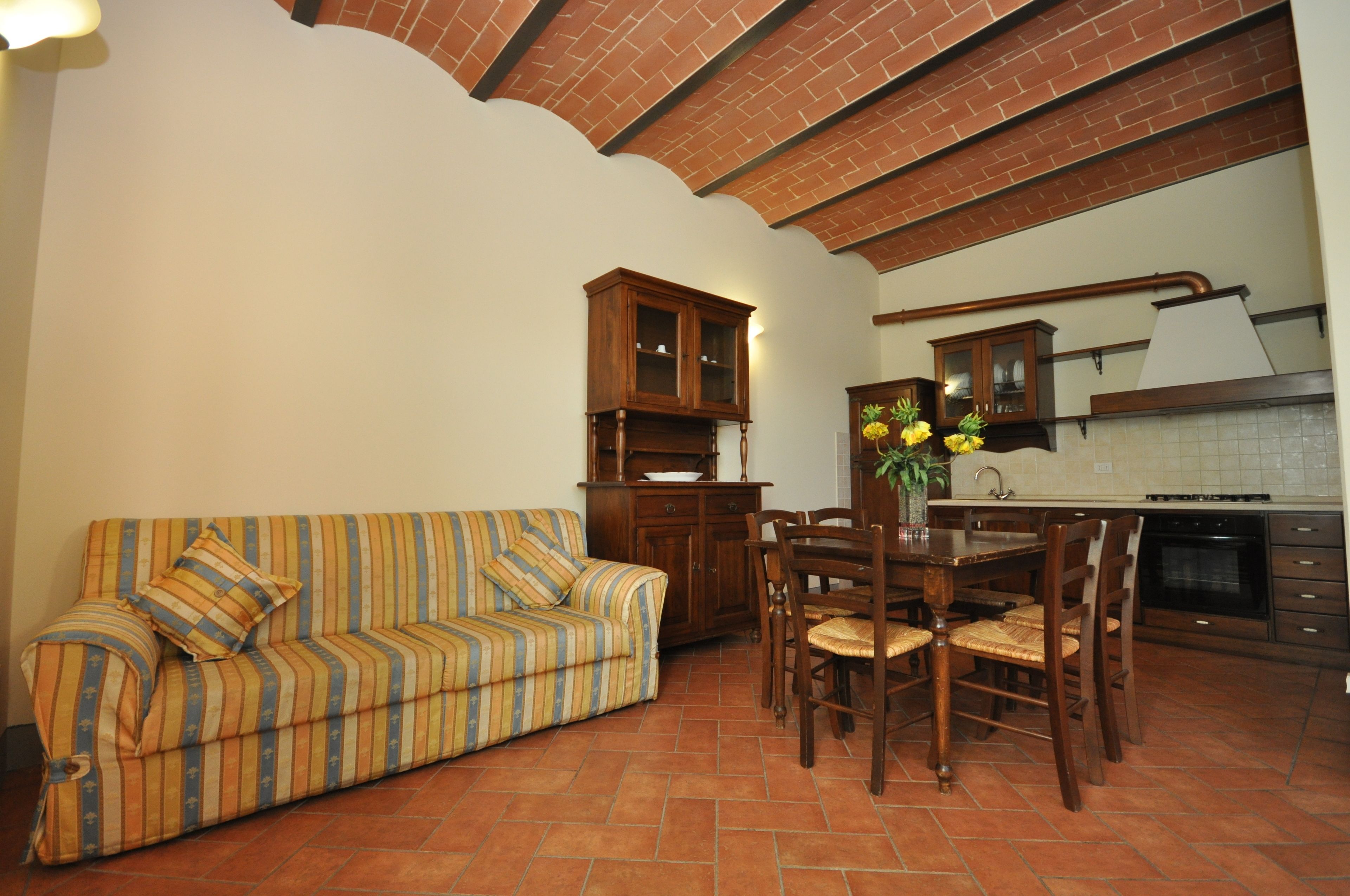 A living room with a striped sofa, wooden dining table, chairs, and a kitchen area with a stove and cabinets.