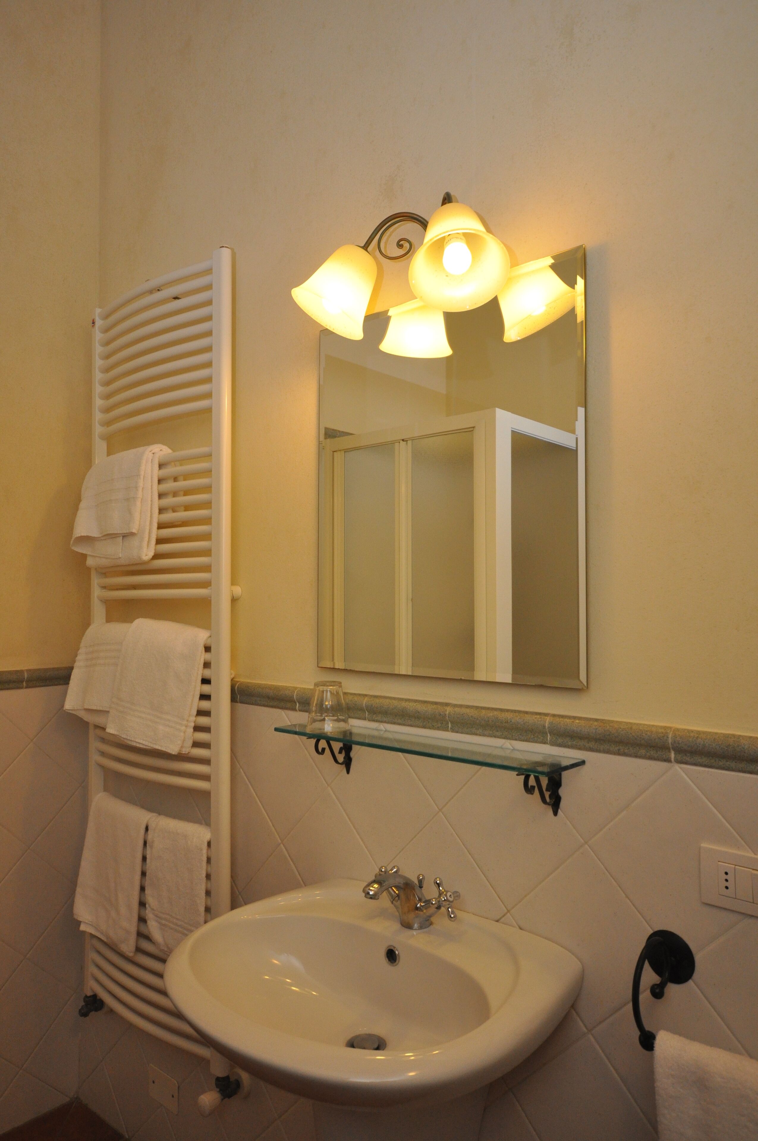 Un baño con lavamanos blanco, un espejo con lámpara y un perchero con toallas.