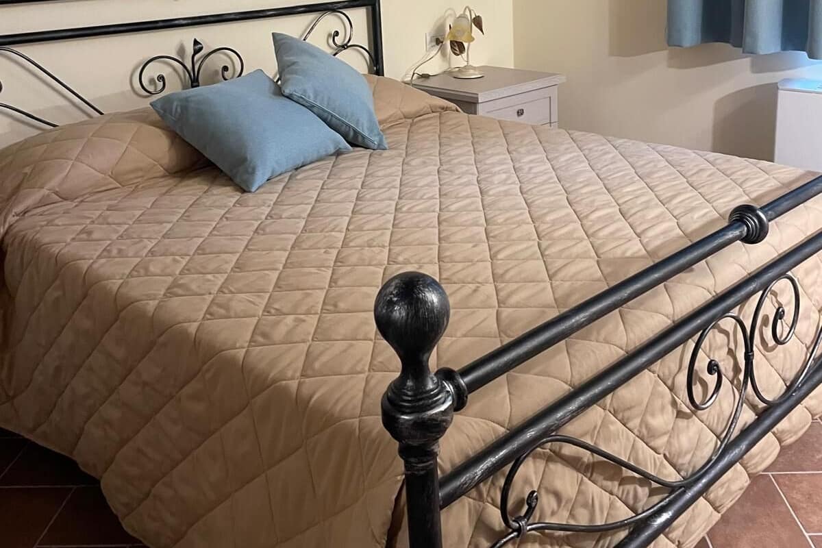 A bed with a beige quilted bedspread, a black metal frame, and two pillows.