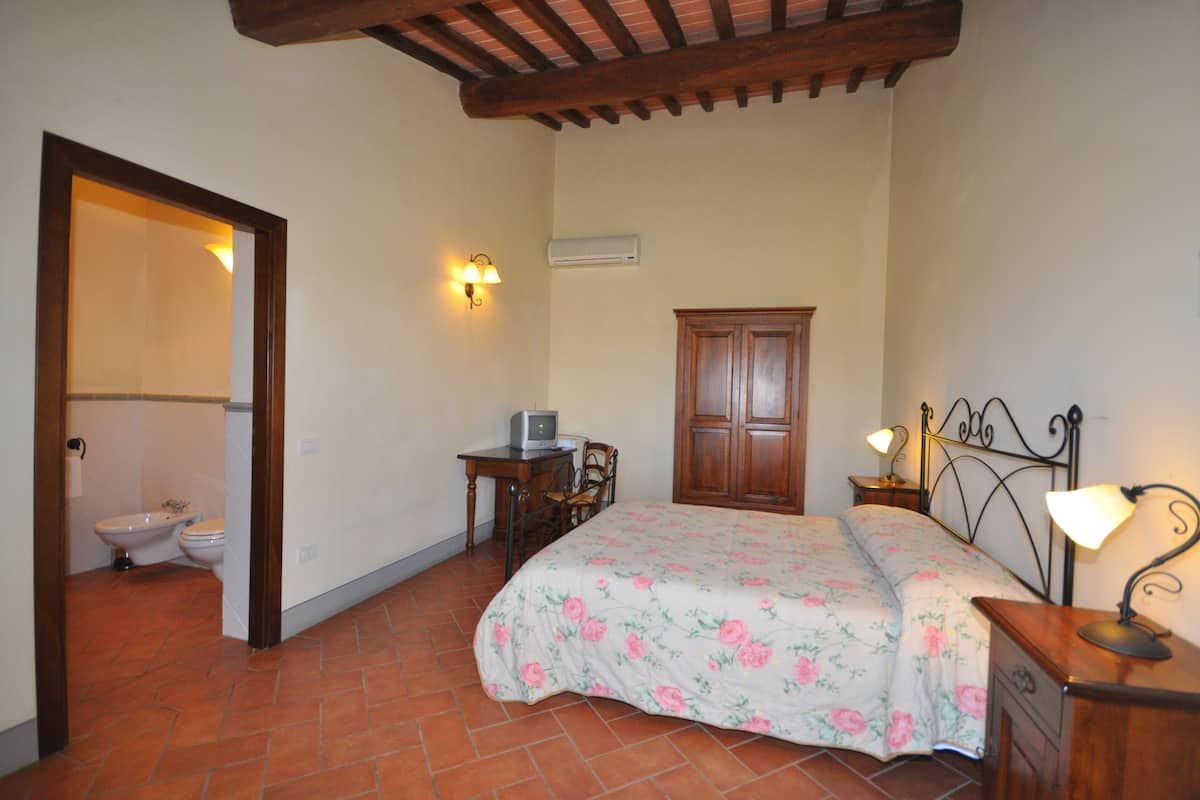 A bedroom with a bed, a desk with a computer, a chair, a wardrobe, and a bathroom with a toilet and bidet.