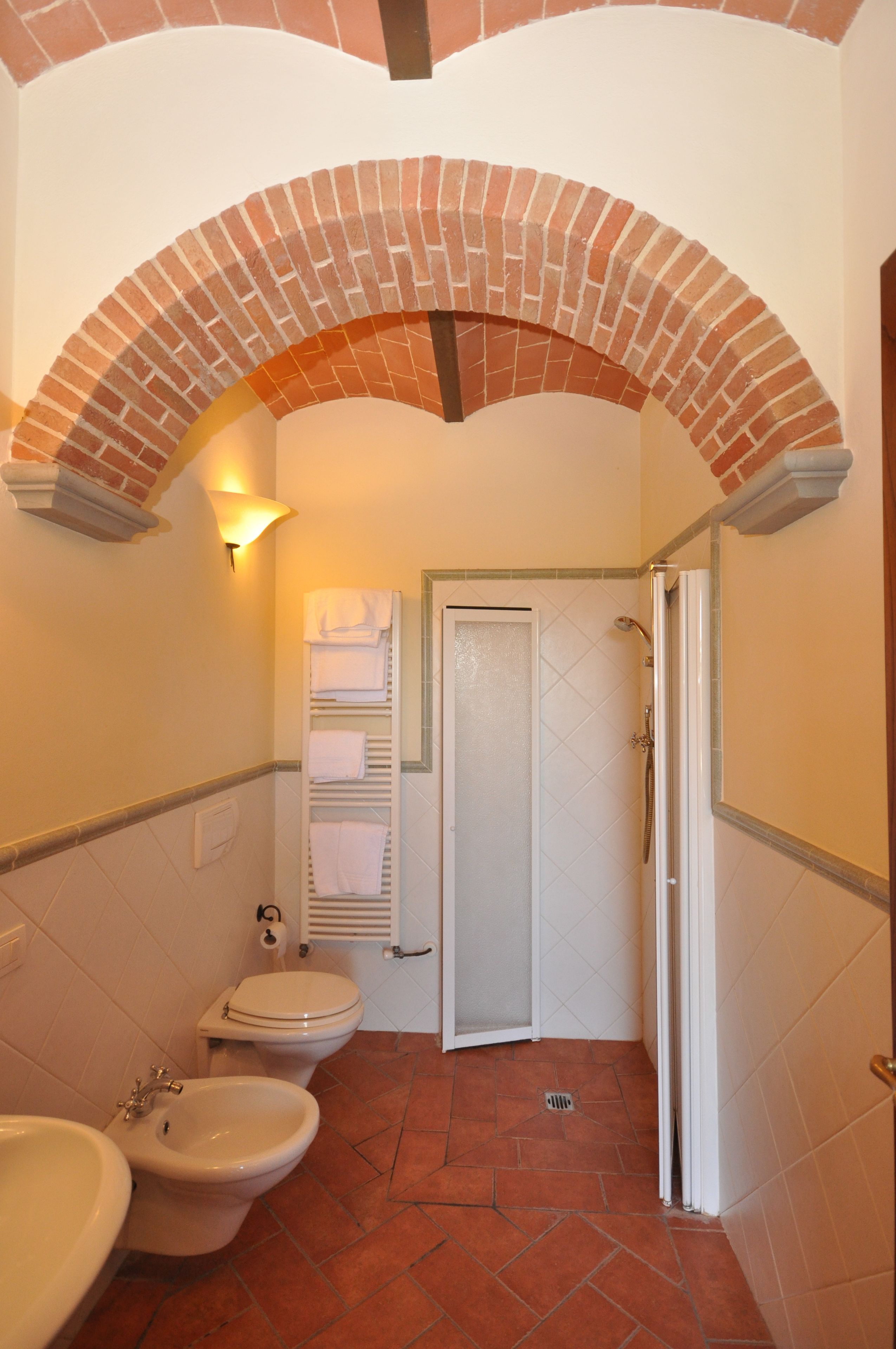 Une salle de bain avec des toilettes, un bidet et un lavabo blancs, un porte-serviettes et un espace douche.