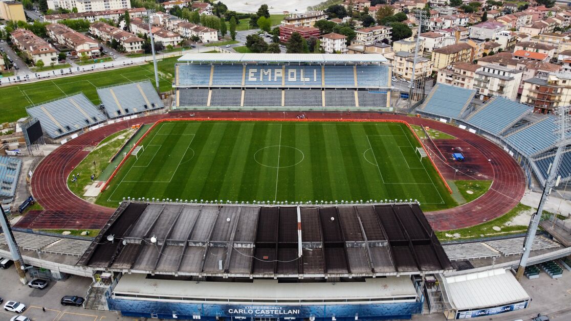 An aerial view of a stadium with "EMPOLI" written on the stands, surrounded by residential buildings.