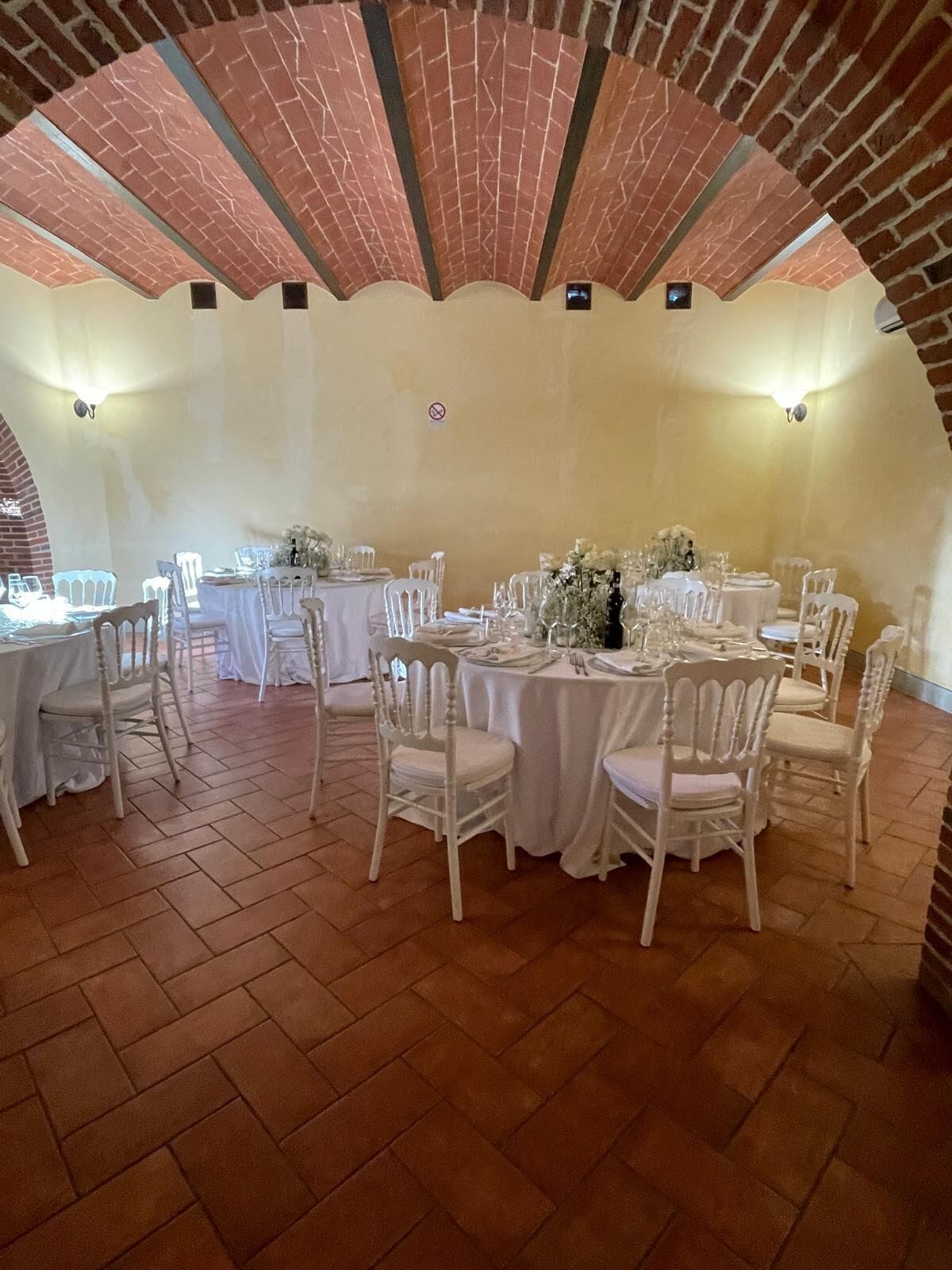 Un salón de banquetes con mesas redondas, sillas blancas y arcos de ladrillo.