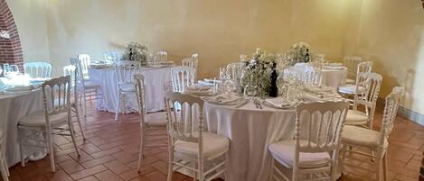 Un salón de banquetes con mesas redondas, sillas blancas y arcos de ladrillo.