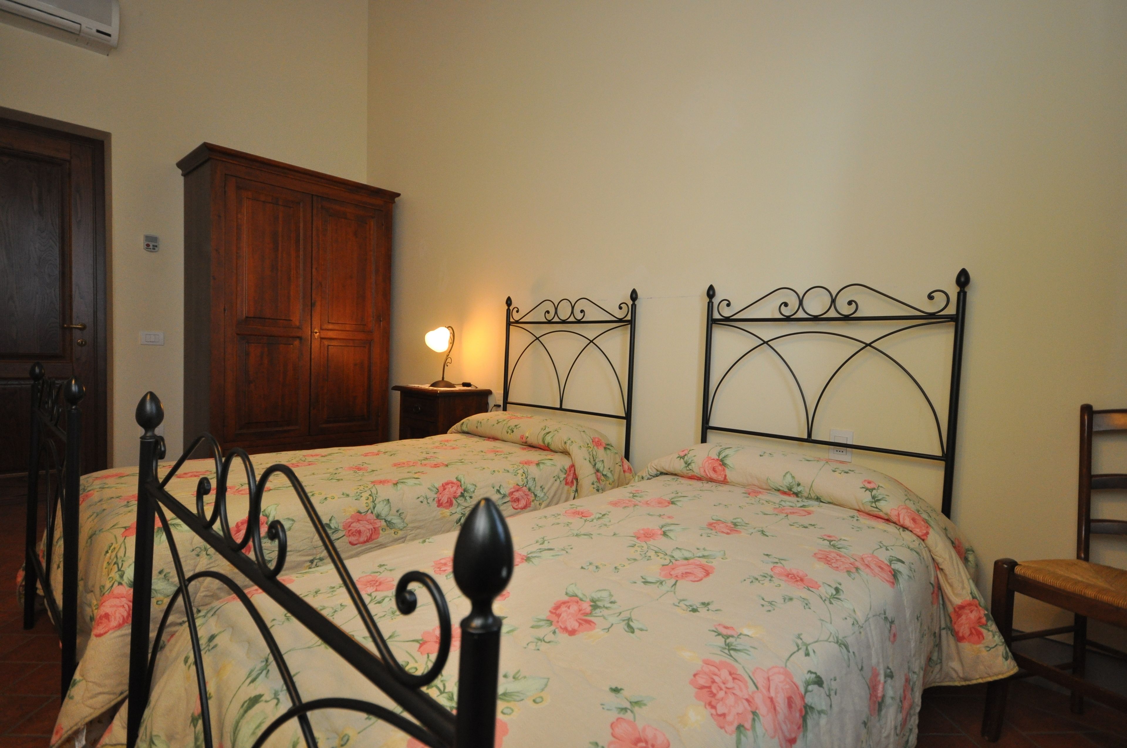A bedroom with two single beds, a wooden wardrobe, and a bedside table with a lamp.