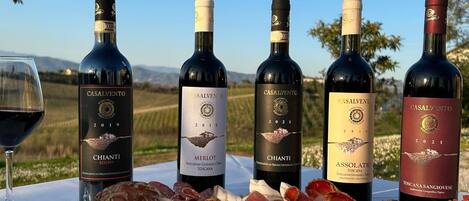 A table set outdoors with wine bottles, charcuterie, and cheese.