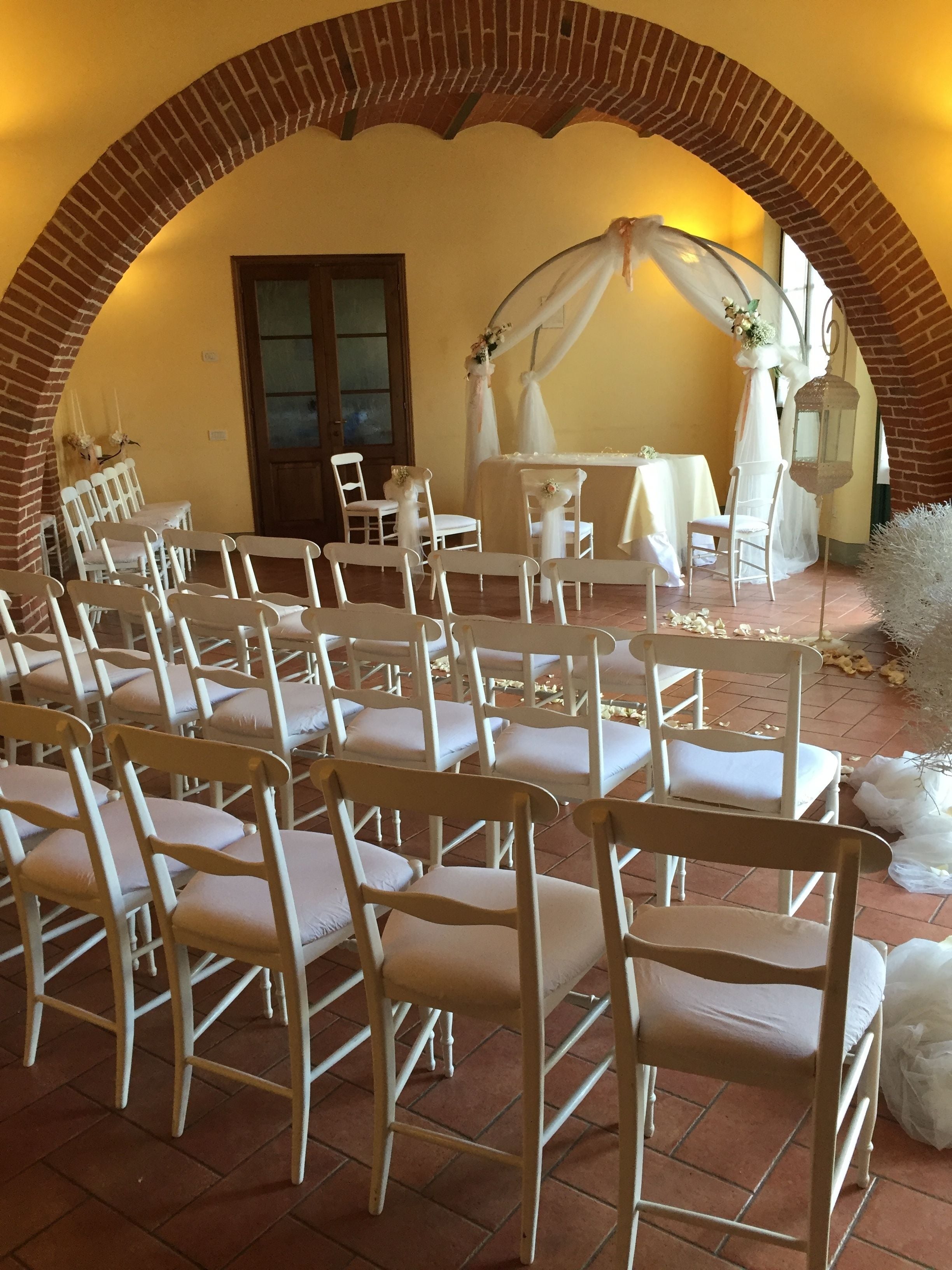 Un lieu de réception en plein air pour un mariage, avec des chaises blanches disposées en rangées, une arche décorée et une table préparée pour la cérémonie.