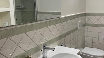 A bathroom with a white sink, two toilets, and a glass shower enclosure.