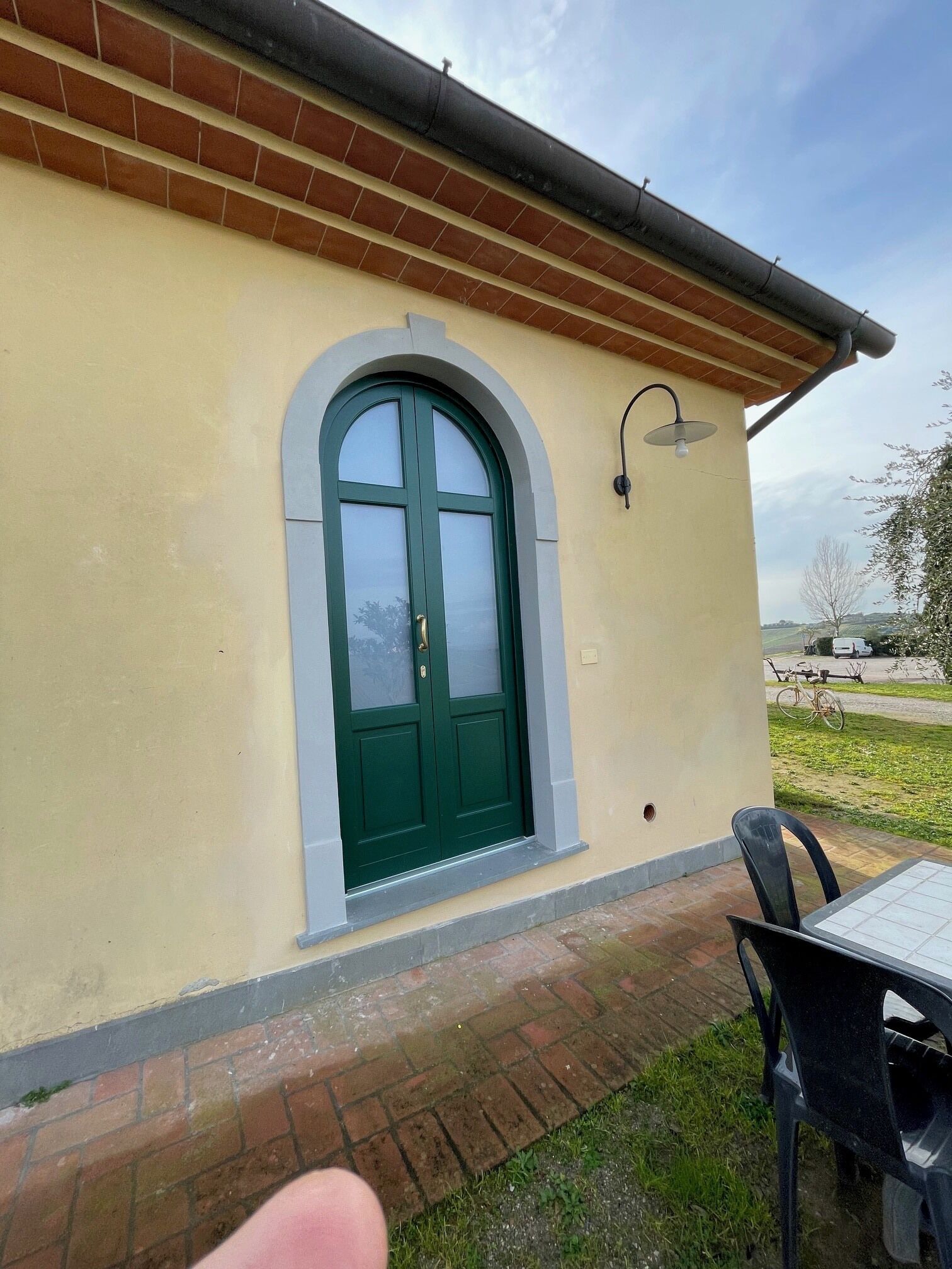 A building with a green door and a small window, a brick pathway, and a table with chairs outside.