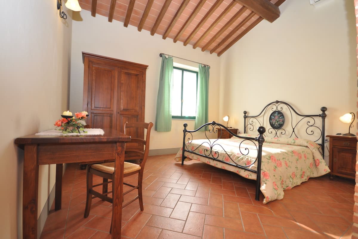 A bedroom with a bed, a wooden desk, a chair, and a window with curtains.