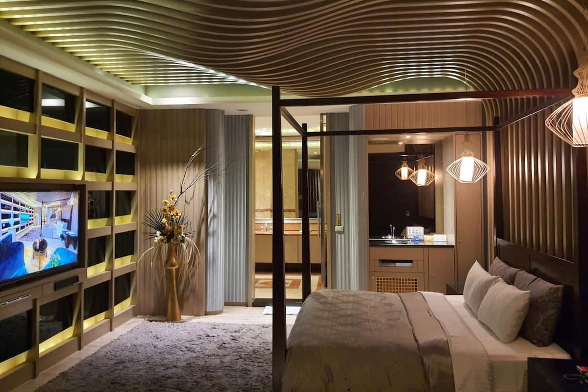 A modern hotel room with a large TV, a bed, a desk, and a bathroom.