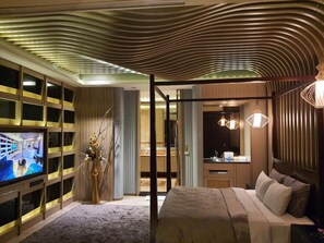 A modern hotel room with a large TV, a bed, a desk, and a bathroom.