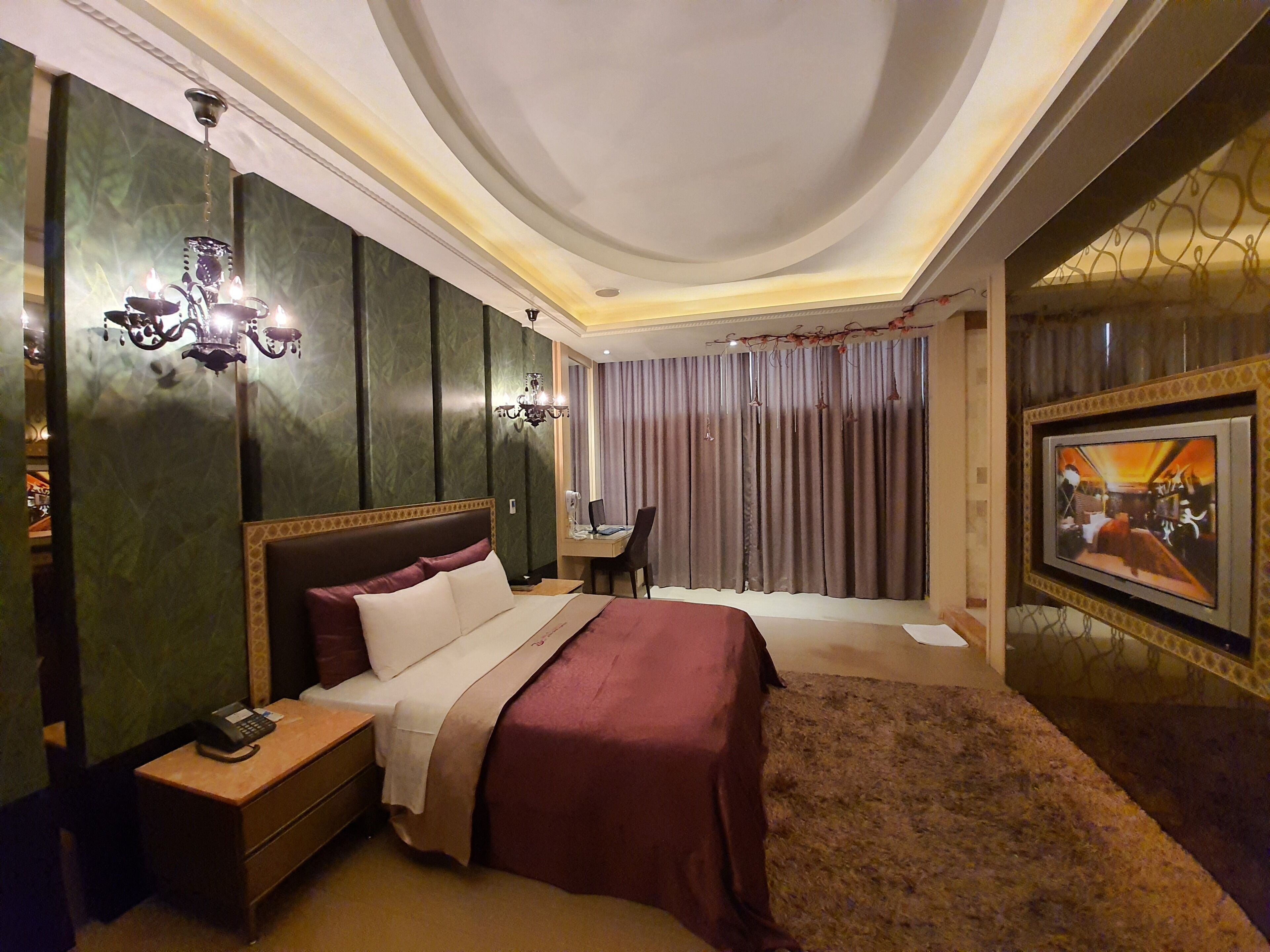 Ein Hotelzimmer mit einem großen Bett, einem Schreibtisch mit Telefon, einem Sessel, einem Fernseher und einem Vorhang.