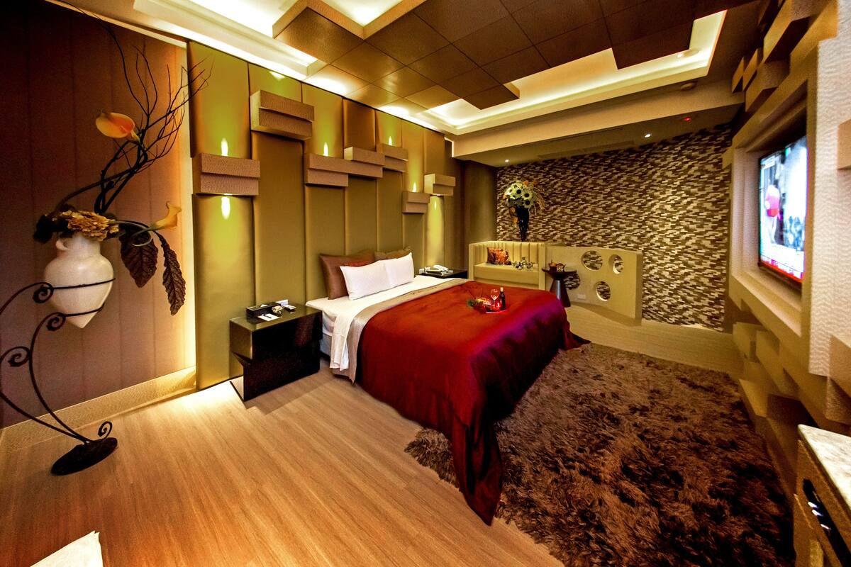 A modern hotel room with a large bed, a nightstand, a decorative vase, and a television on the wall.