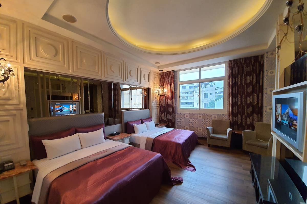 A hotel room with two beds, a TV, a desk, and a window with a city view.