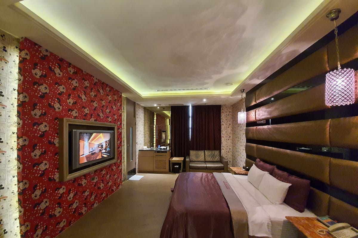 A hotel room with a large bed, a TV mounted on the wall, a small desk, and a sofa.