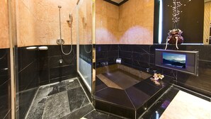 A modern bathroom with a glass shower enclosure, black and beige tiled walls, and a mounted television. - Jin Sha Motel (Taichung)