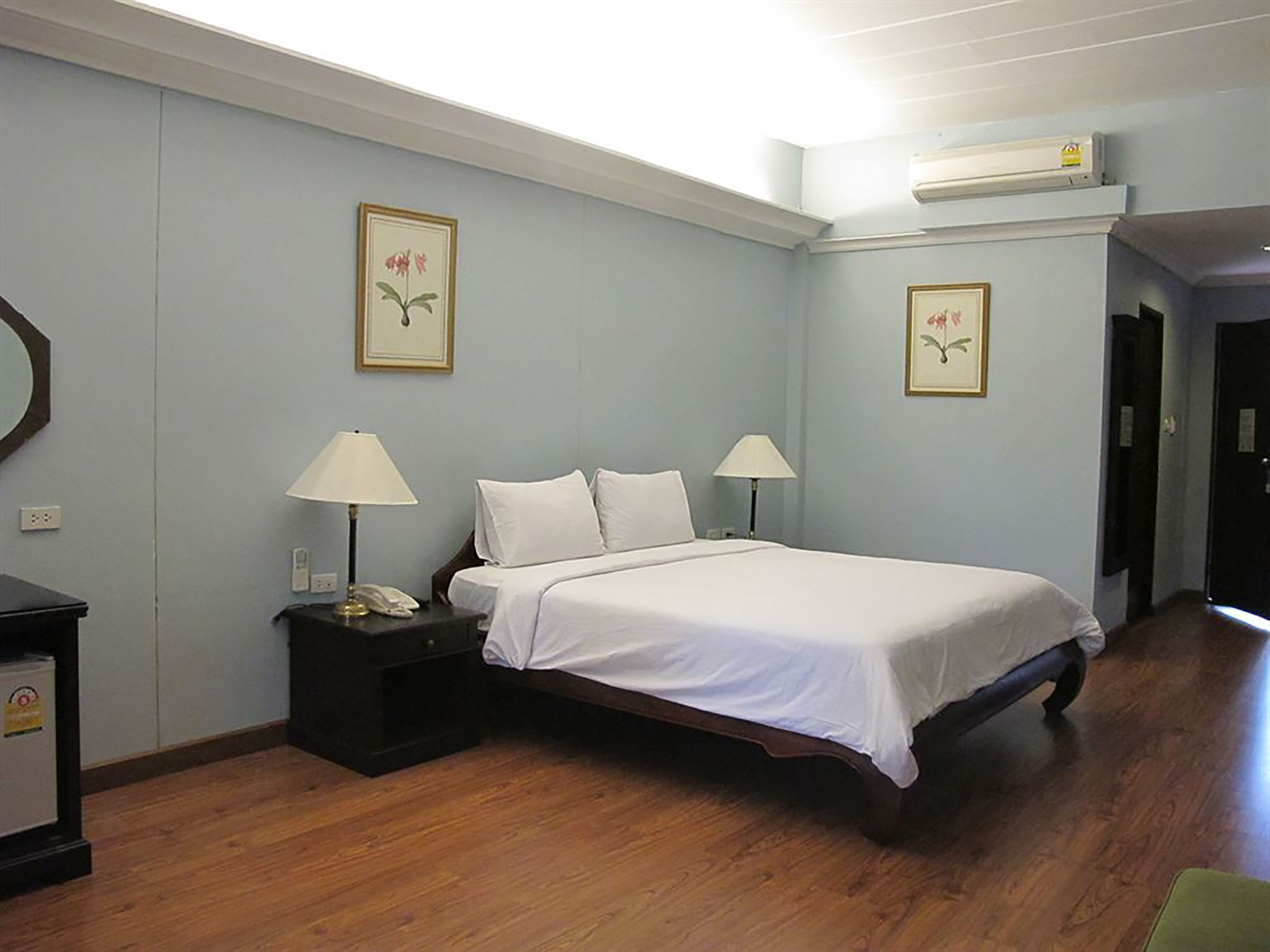 A hotel room with a bed, bedside lamps, a nightstand, a mirror, and two framed floral pictures on the wall.