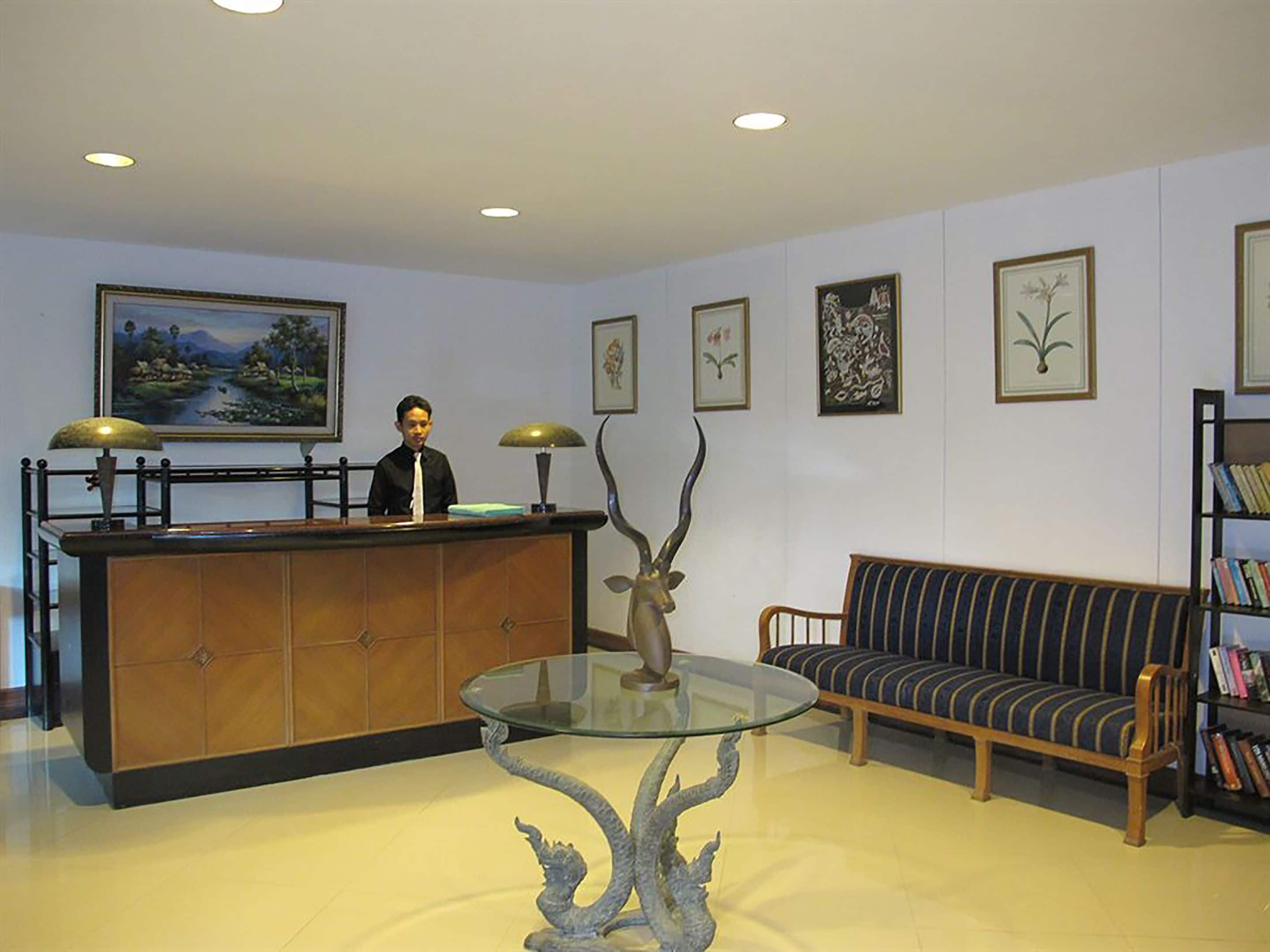 A reception area with a receptionist, a reception desk, a glass-top table with a decorative sculpture, a striped sofa, and framed artwork on the walls.