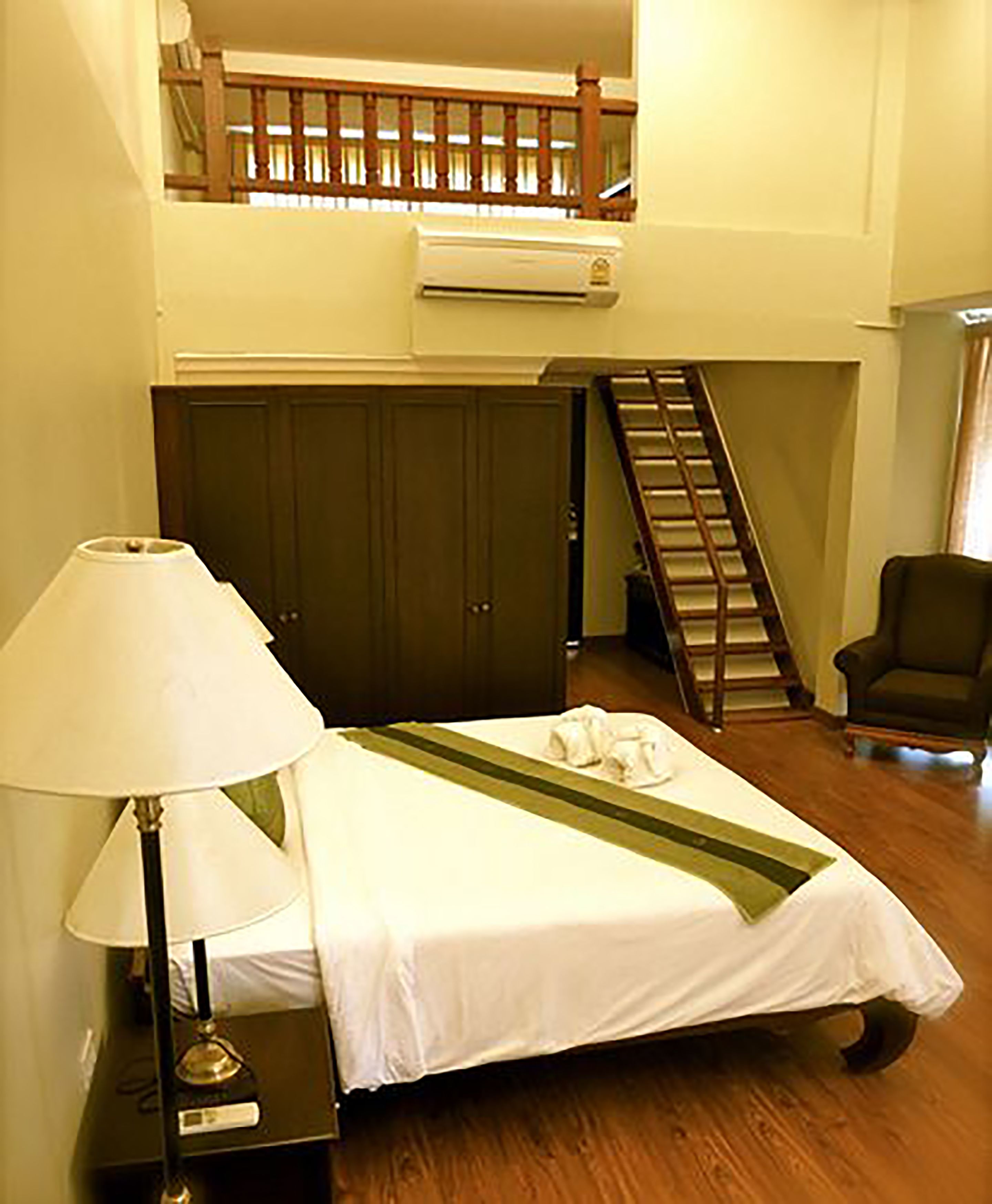 A hotel room with a bed, a lamp, a chair, a wardrobe, and a staircase.