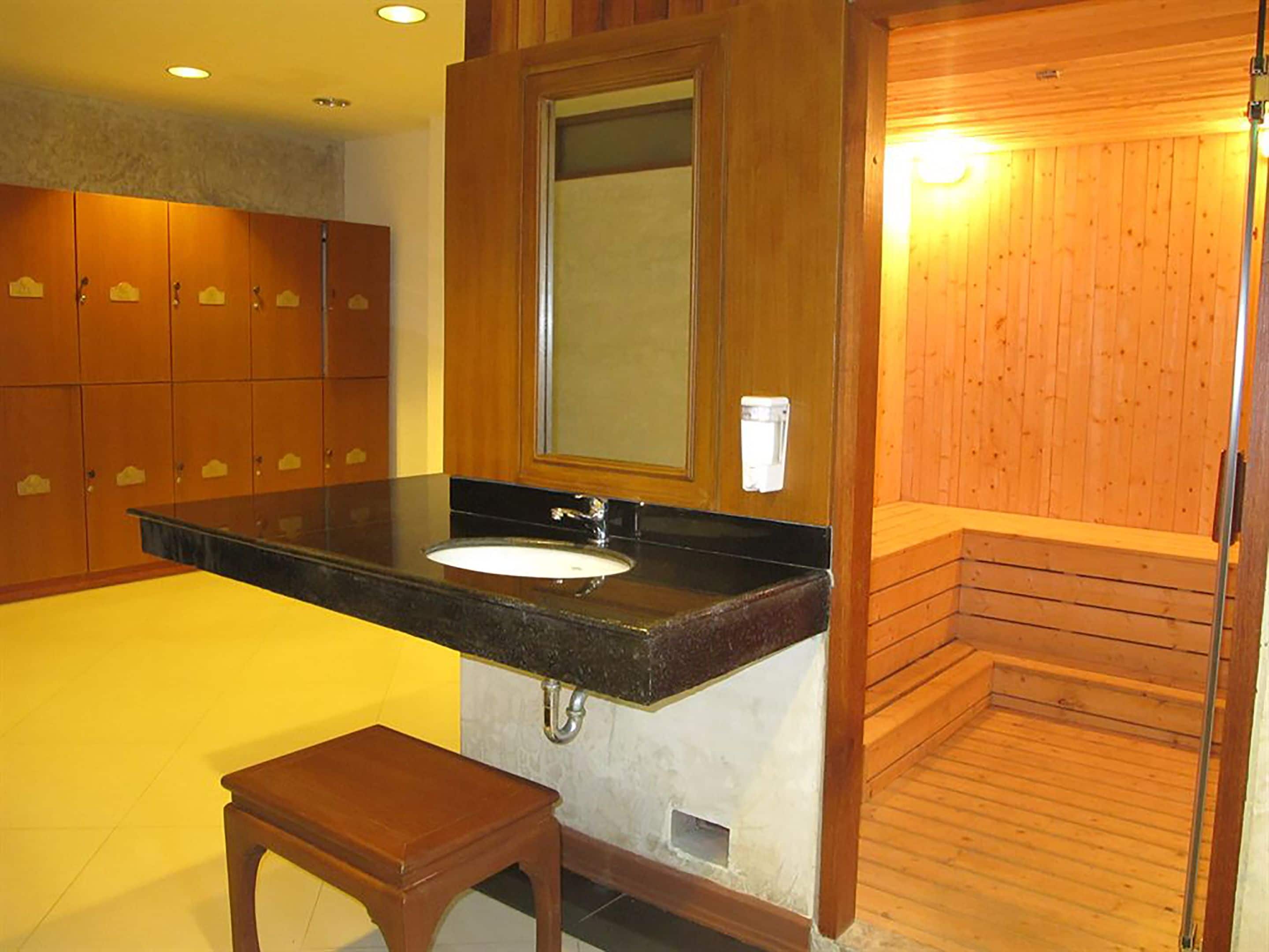 Un baño con tocador de madera, lavamanos, espejo y banco.