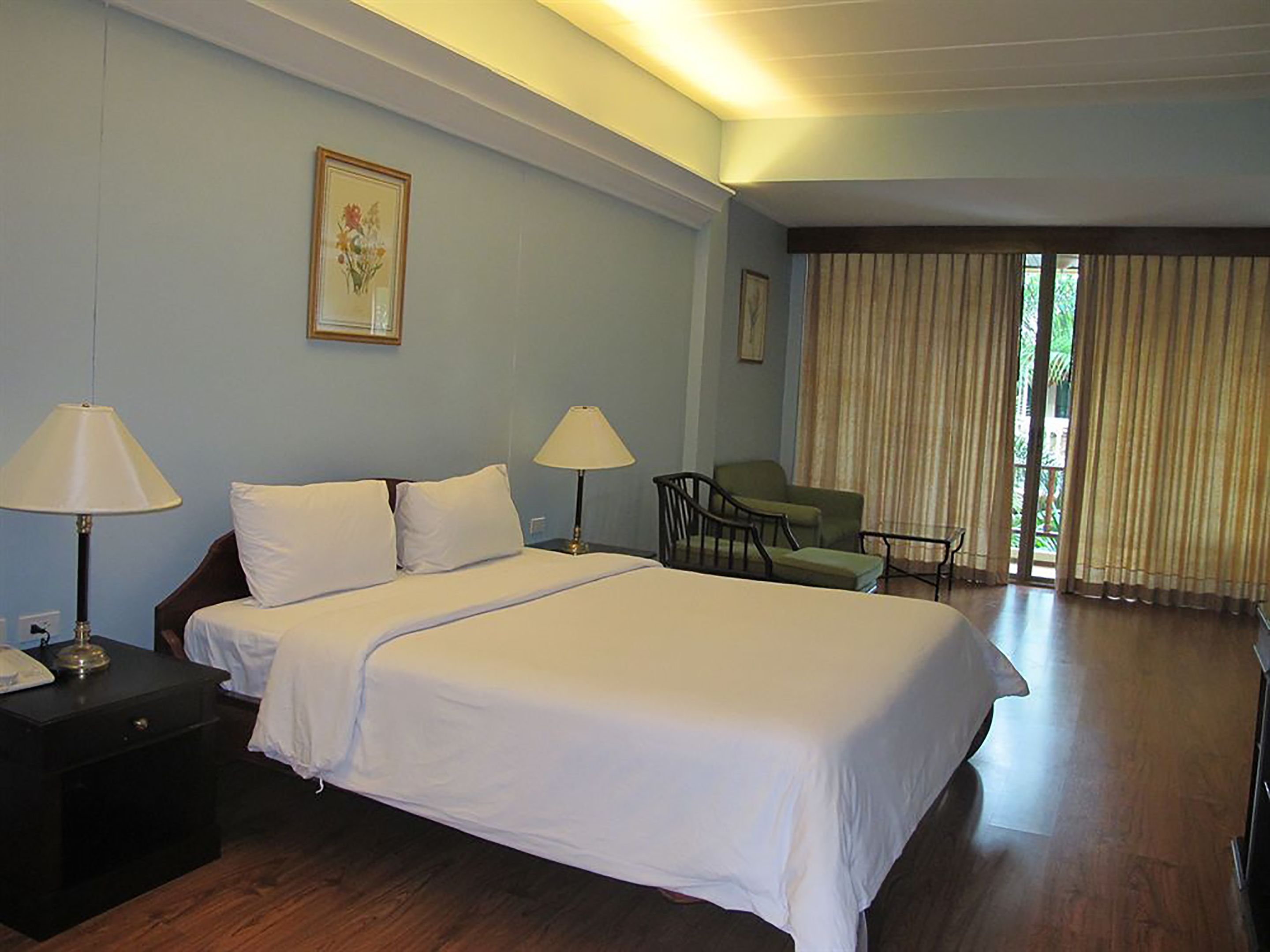 Une chambre d’hôtel avec un grand lit, deux lampes de chevet, une chaise et une fenêtre avec des rideaux.