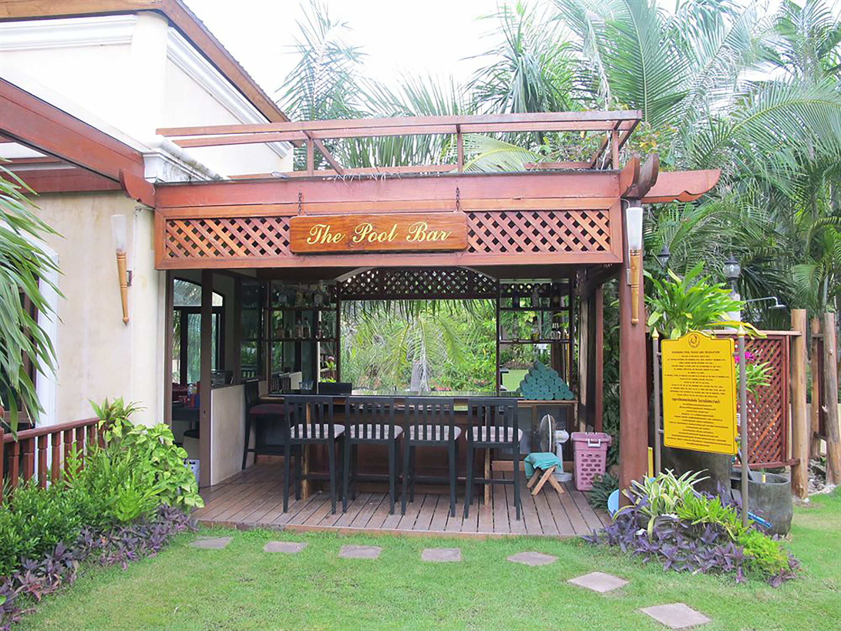Un bar junto a la piscina con asientos exteriores y un cartel arriba.